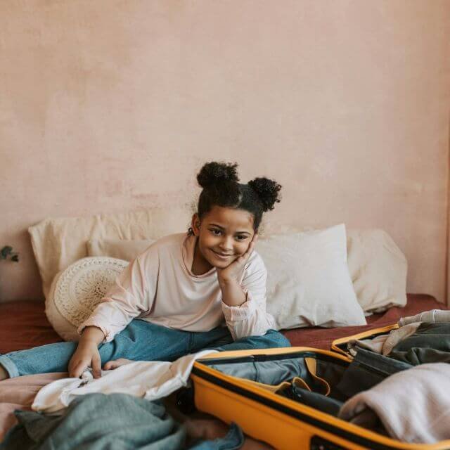 petite fille rêvant à son futur voyage en famille devant sa valise en préparation