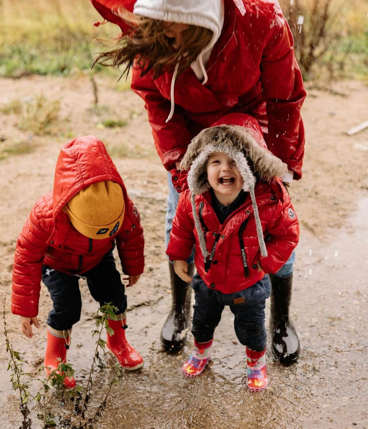 deux enfants et leur mère bien couverts jouant sous la pluie