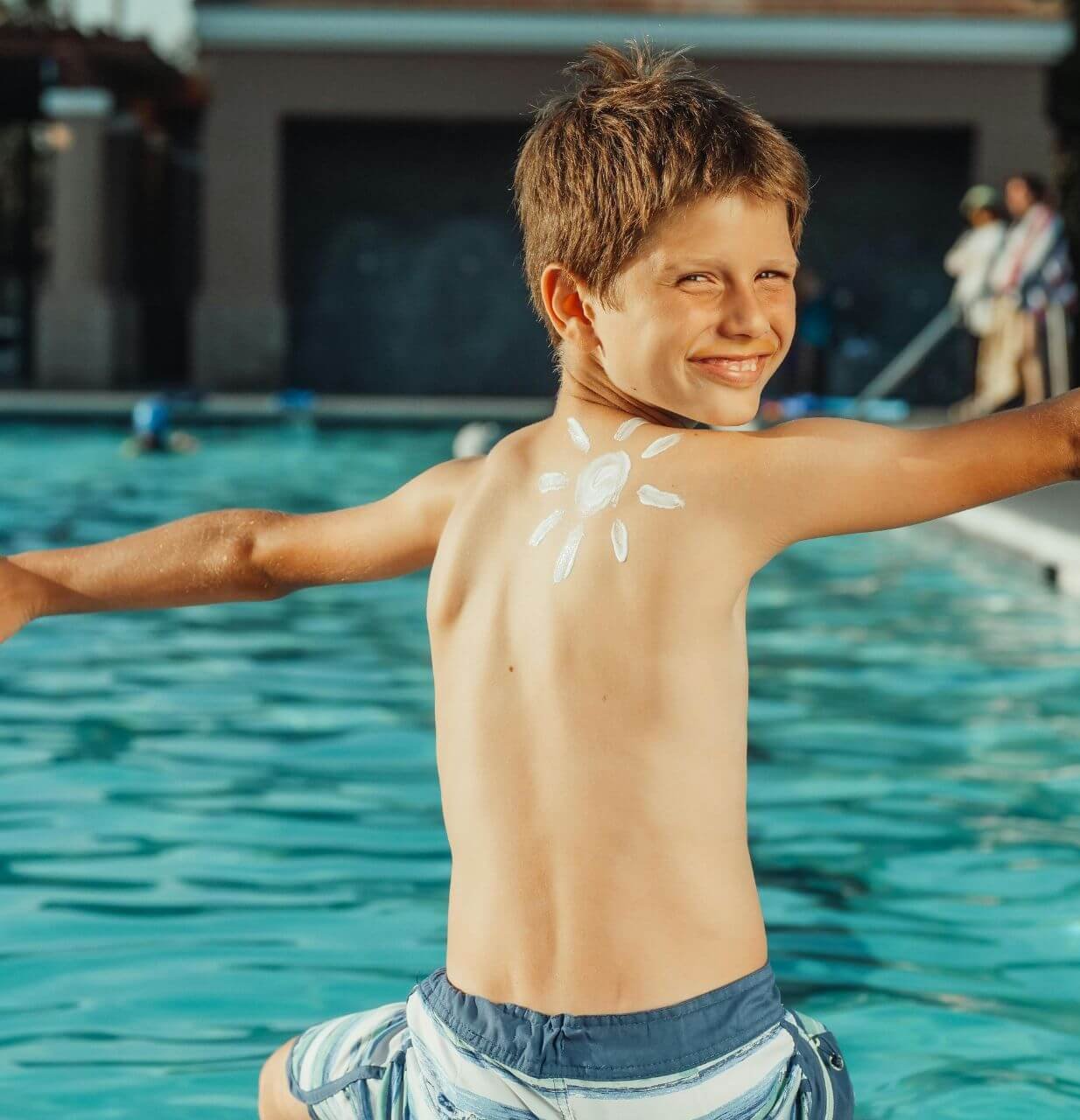 enfant assis au bord d'une piscine avec un soleil déssiné sur le dos avec de la crème solaire