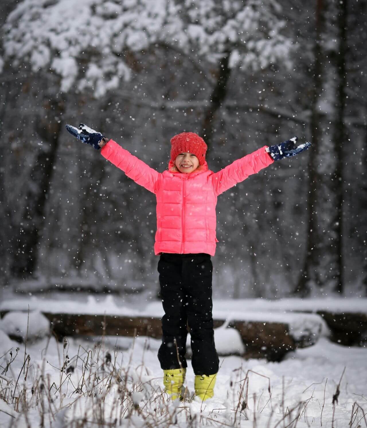 enfant bien équipé pour le grand froid qui sourie et léve les bras de bonheur d'être sous la neige qui tombe