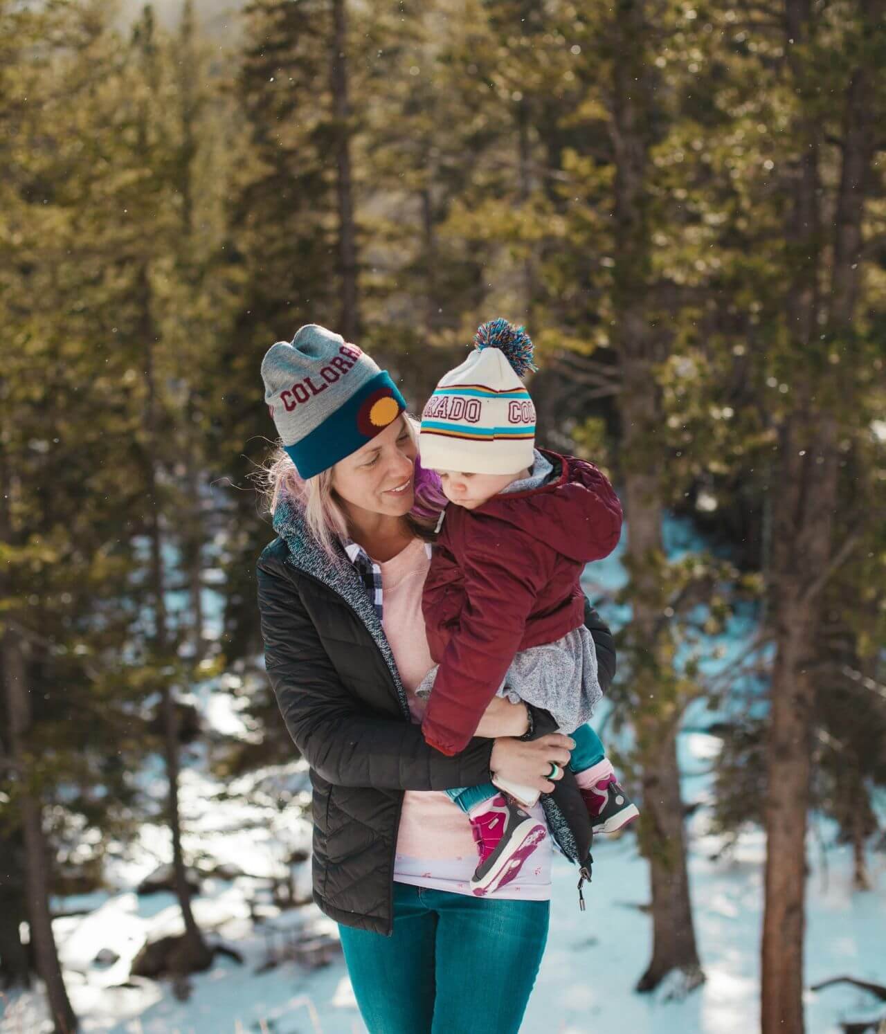 mère avec son bébé dans les bras bien couvert pour une promenade dans une fôret enneigée